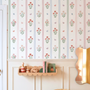 Girls bedroom wall with vintage floral stripe wallpaper wooden toy shelf mirror and pastel nursery decor.
