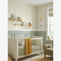 “Nursery room with cream striped wallpaper featuring small cars and balloons, white crib, sage green armchair, and soft textured accessories.”