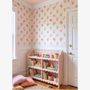 Cottagecore girls playroom with pink floral stripe wallpaper and scalloped bookshelf filled with children's books.