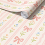 Close up of pink bow floral wallpaper roll showing textured matte finish, pastel stripe nursery wallpaper with flowers and ribbons