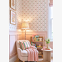 Cozy nursery reading corner with floral stripe wallpaper armchair pastel cushion wooden bookshelf and children's books.
