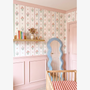 Girls nursery with vintage floral stripe wallpaper pink wall paneling wooden crib and pastel wavy mirror.