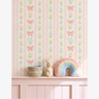 Pink striped bow wallpaper with floral pattern in nursery shelf styling, pastel rainbow cushion and bunny decor, soft girl room aesthetic