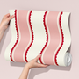 Red and pink scalloped stripe wallpaper sample held in hands, playful kids room wallpaper with wavy stripe pattern