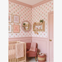 Vintage rose floral stripe wallpaper in pink nursery with blush wall paneling crib and cozy reading chair.