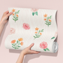 Roll of wallpaper with floral design held by a hand on a pink background