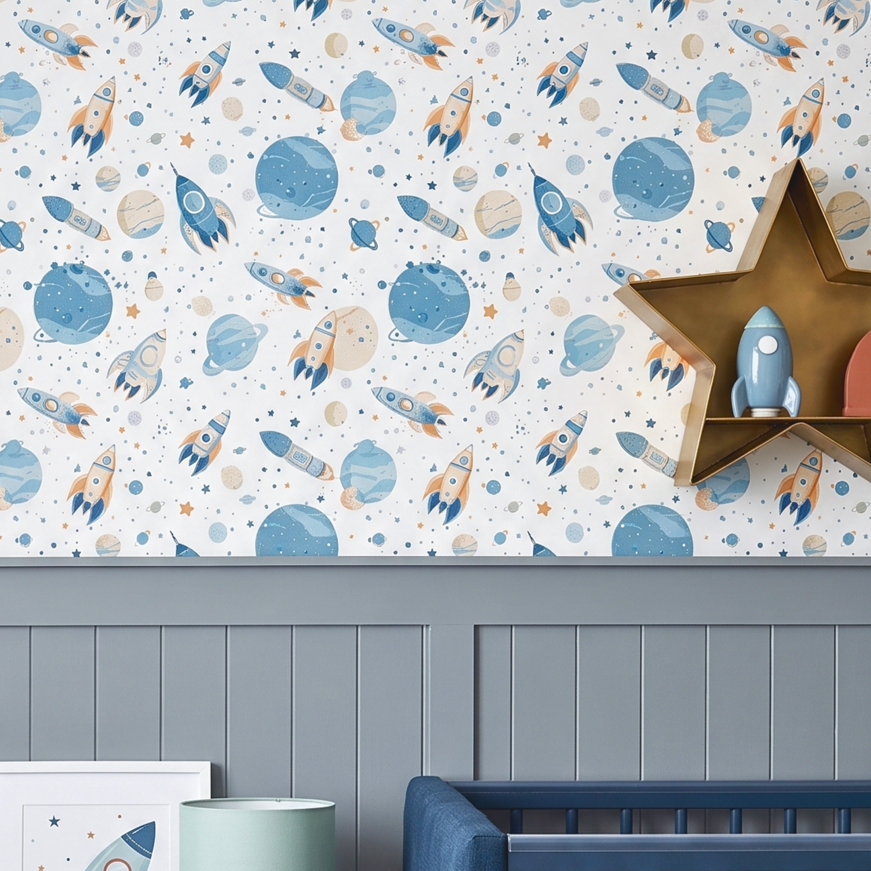A children's nursery wall decorated with a white wallpaper featuring a playful space pattern of blue planets, rockets, and stars. The wall is styled above a gray paneled wainscoting, with a wooden star shelf holding a small blue toy rocket.